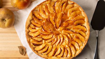 Glasierter Apfelkuchen auf einem Tisch, frische Äpfel daneben