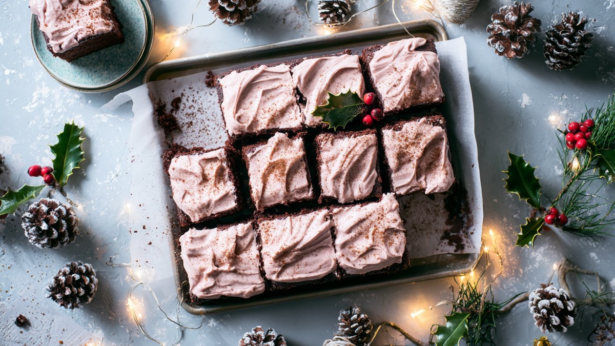Draufsicht: ein Glühweinkuchen vom Blech mit Frosting. Ringsum liegen Kiefernzapfen und Stechpalmenzweige. Außerdem liegt eine Lichterkette drapiert rund ums Blech. Weihnachtliches Ambiente.