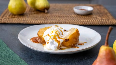 Ein Teller mit einer angerichteten holländischen Birne. Im Hintergrund kann man auf einem Tischuntersetzer Birnen und eine Schale mit Gewürz erkennen. Im Vordergrund ragen auch Birnen ins Bild.