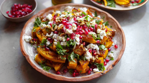 Ein bunter Teller mit libanesischer Kürbissalat. Eine Schale mit Granatapfelkernen steht im Hintergrund.