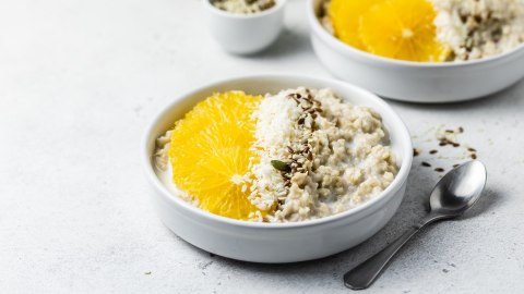 Zwei Schalen Orangen-Porridge, garniert mit Orange und Kernen.