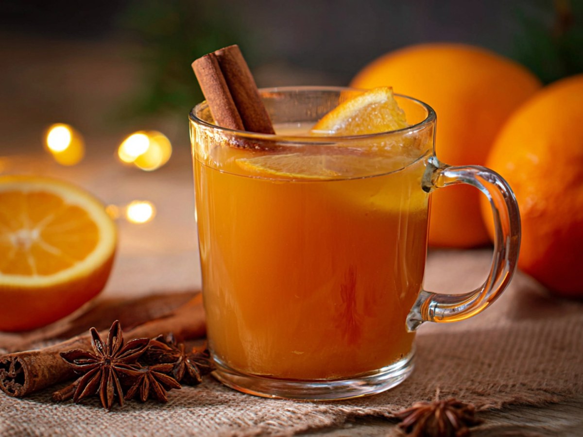 Eine Tasse Orangenpunsch ohne Alkohol, daneben rohe Orangen.