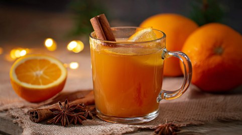 Eine Tasse Orangenpunsch ohne Alkohol, daneben rohe Orangen.
