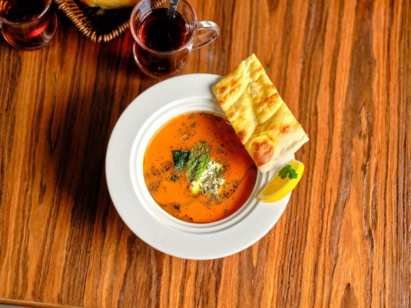 Ein Teller mit türkischer Tarhana-Suppe, garniert mit Kräutern. Ein Stück Fladenbrot liegt am Tellerrand und eine Zitronenspalte.