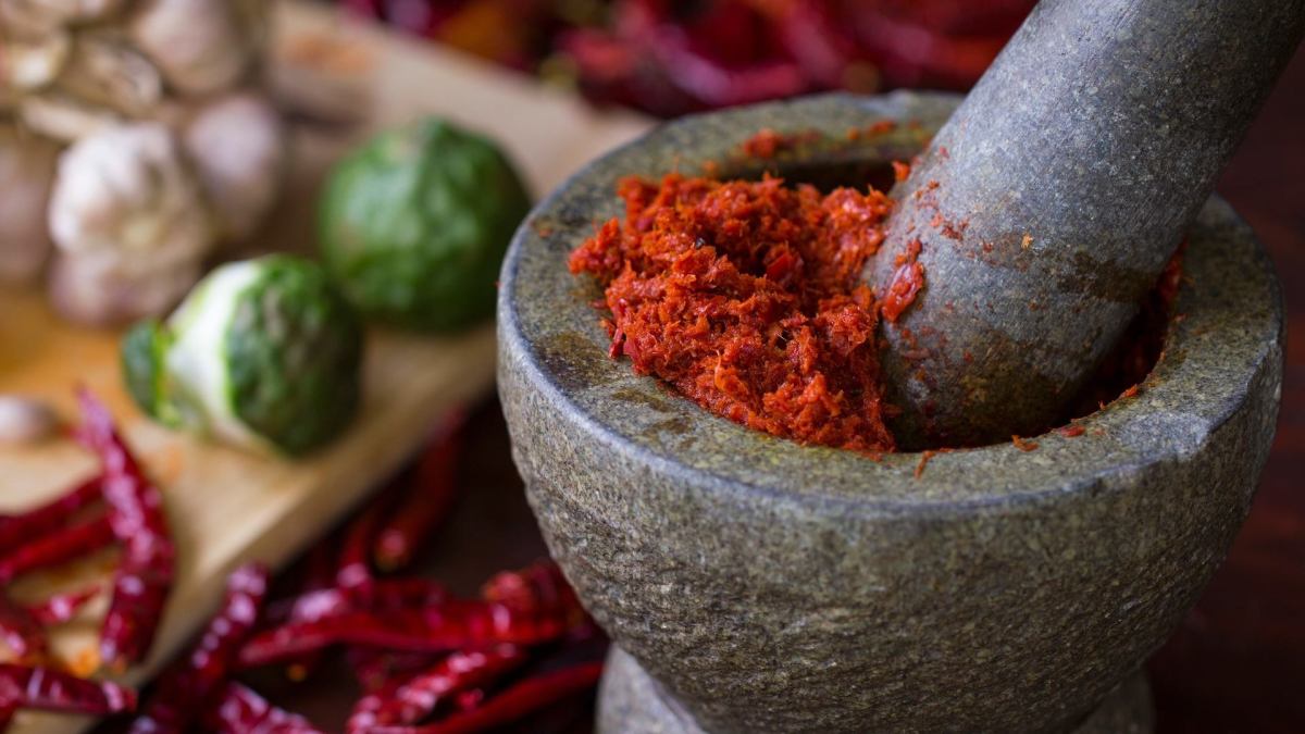 Unterschiede Currypasten: Ein rptes Curry wird in einem Mörser gestampft.